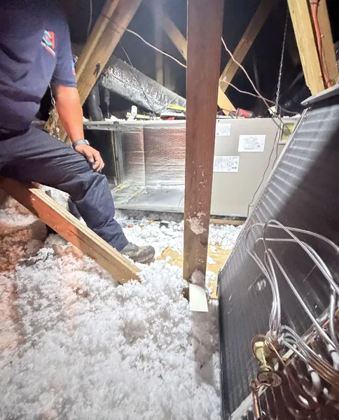 Master Cooling Mechanical technician in a uniform shirt working in an insulated attic next to the air handler, with copper coil tubing in the foreground