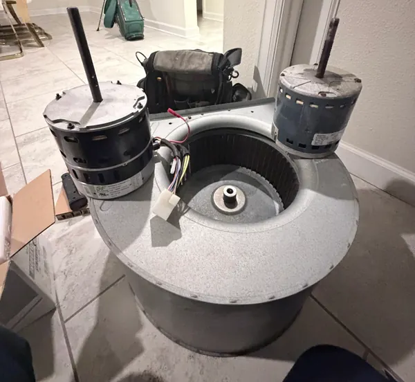 Two indoor blower motors, the old one and its replacement, sitting on top of a removed blower wheel housing