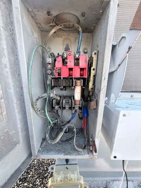 Open outdoor AC electrical disconnect box with burnt, corroded terminals, discolored wiring and a fuse inside