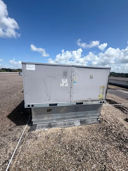 Gray commercial rooftop package air conditioning unit on a flat gravel roof under a blue sky with clouds