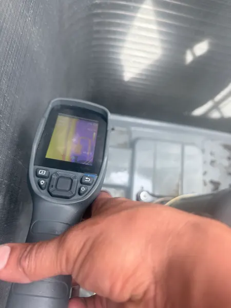 Hand holding a thermal imaging camera up to an AC coil, with a heat image showing on the camera screen